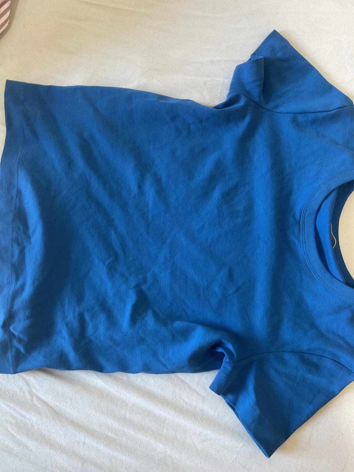 Plain blue short-sleeved T-shirt laid out on a crumpled white fabric surface. Casual and relaxed style composition.
