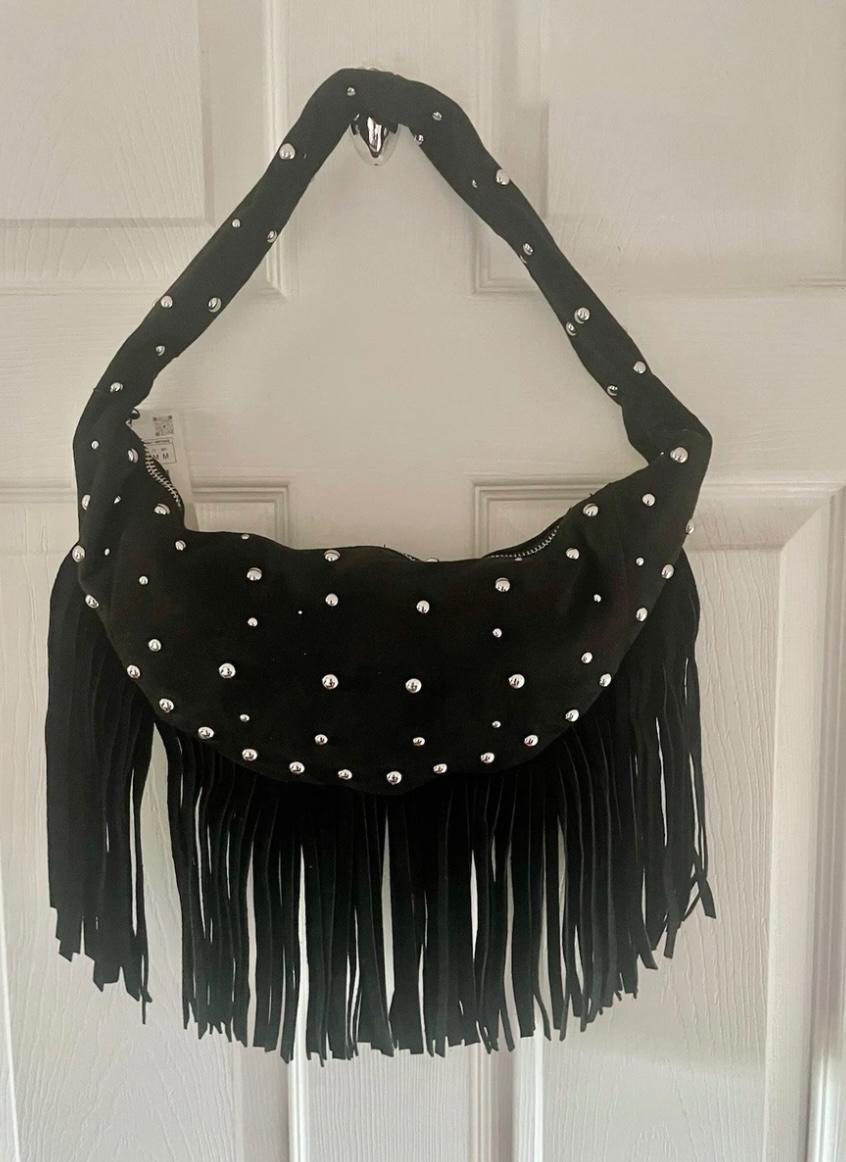 Black bag with silver studs and fringe hanging on a white door. Modern and eye-catching design.