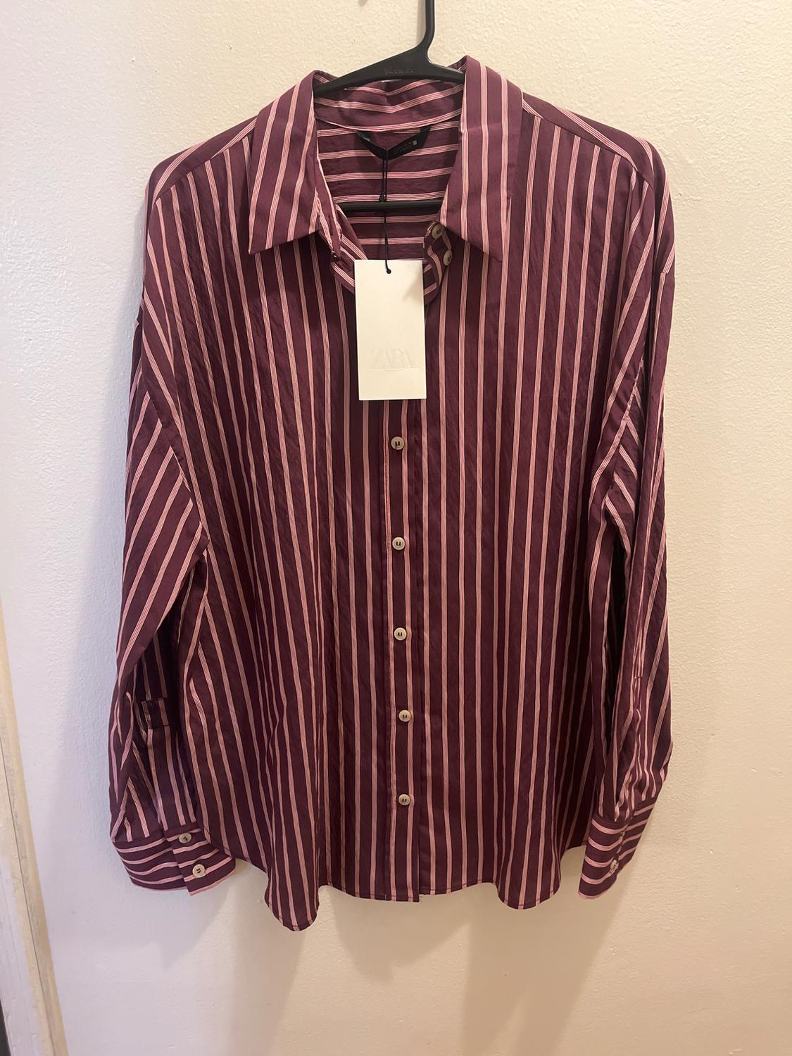 Vertical striped shirt in burgundy and pink tones, hanging on a black hanger. Visible label with the text "ZARA".