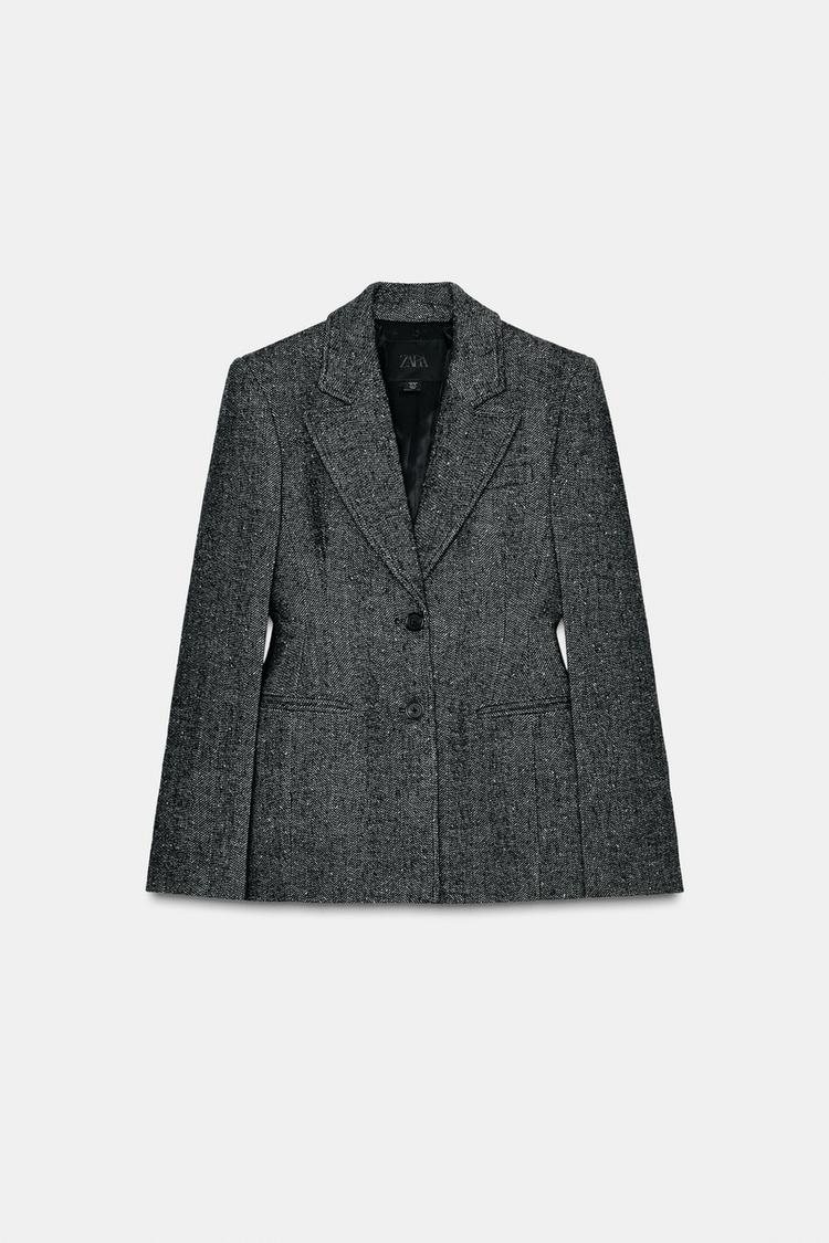Sprednji pogled na črno-bel blazer z ovratnikom z reverjem, dolgimi rokavi in paspuliranimi žepi. Zapenjanje spredaj z gumbom.
