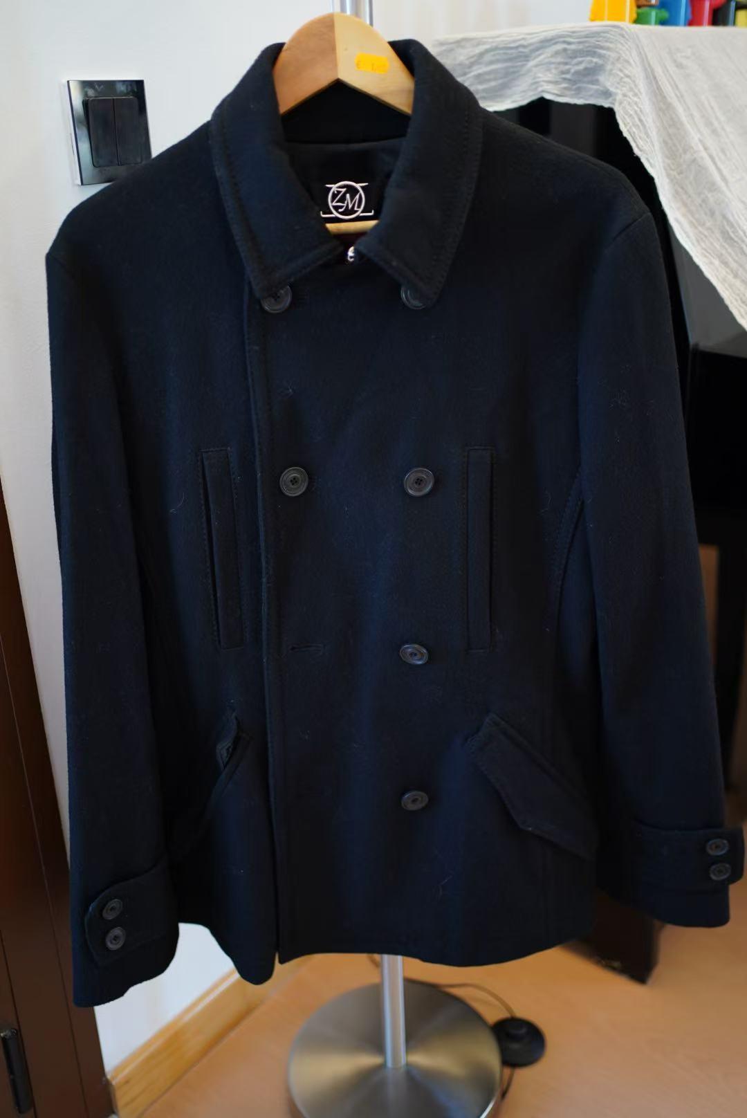 Dark blue double-breasted coat hanging on a wooden hanger, with a white wall background and furniture details.