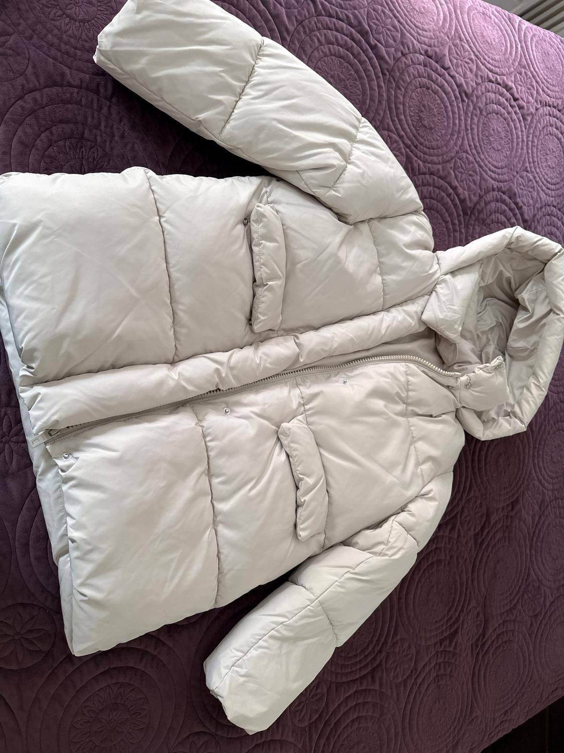 White quilted jacket with hood and zipper closure, on a purple comforter with an embossed circle design.