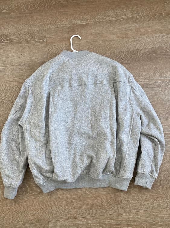 Soft gray fabric jacket hanging on a white hanger over a light wood floor. Rear view of the garment.