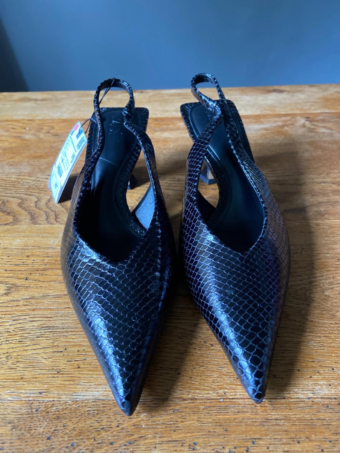Black snake-texture pointed-toe slingback shoes on a wooden table.