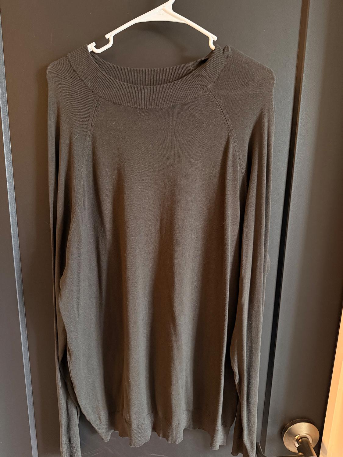 Long-sleeved brown sweater hanging on a white hanger over a dark door.