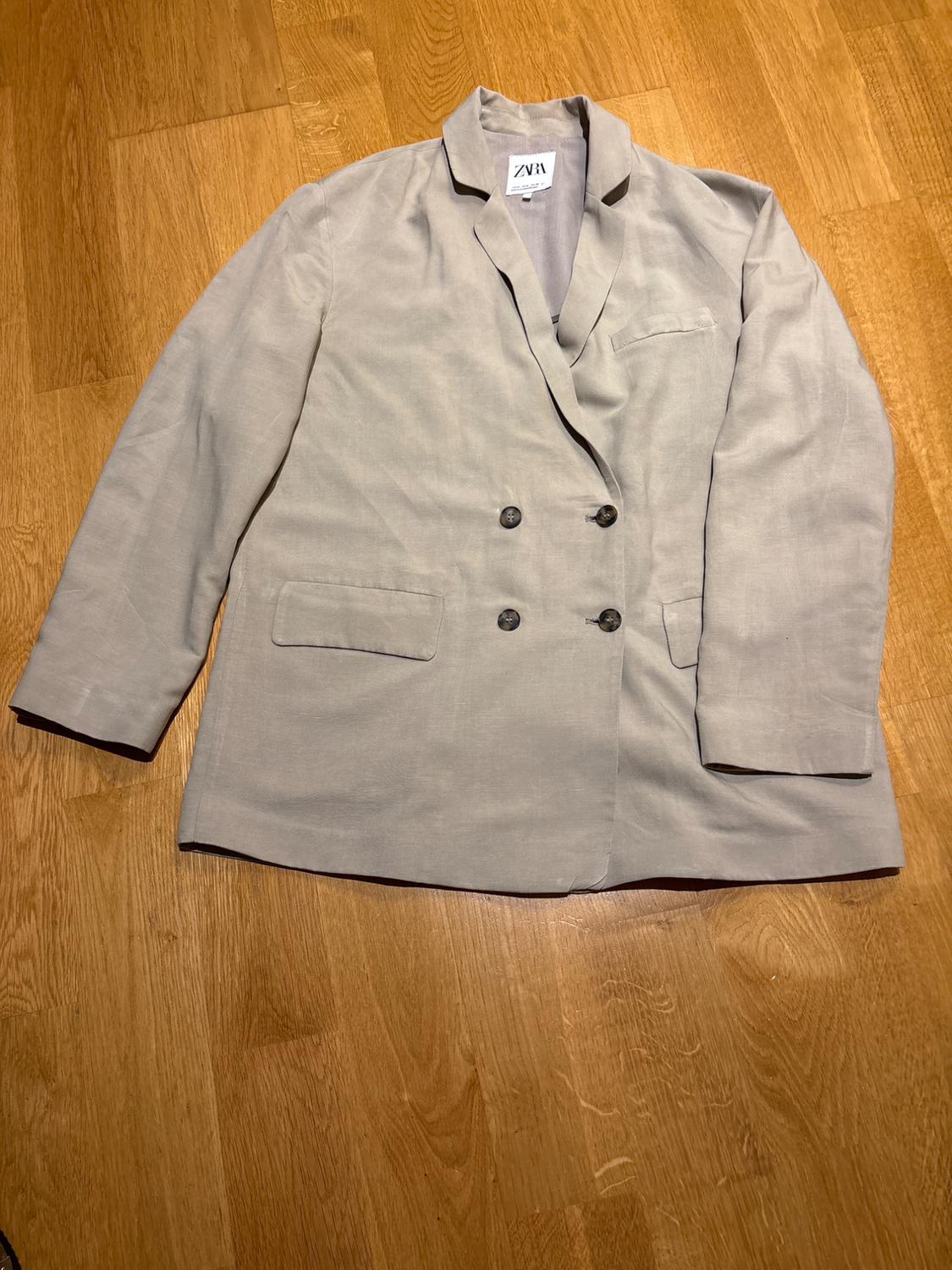 Light grey double-breasted jacket on a wooden floor. Visible label on the collar with the text "ZARA".