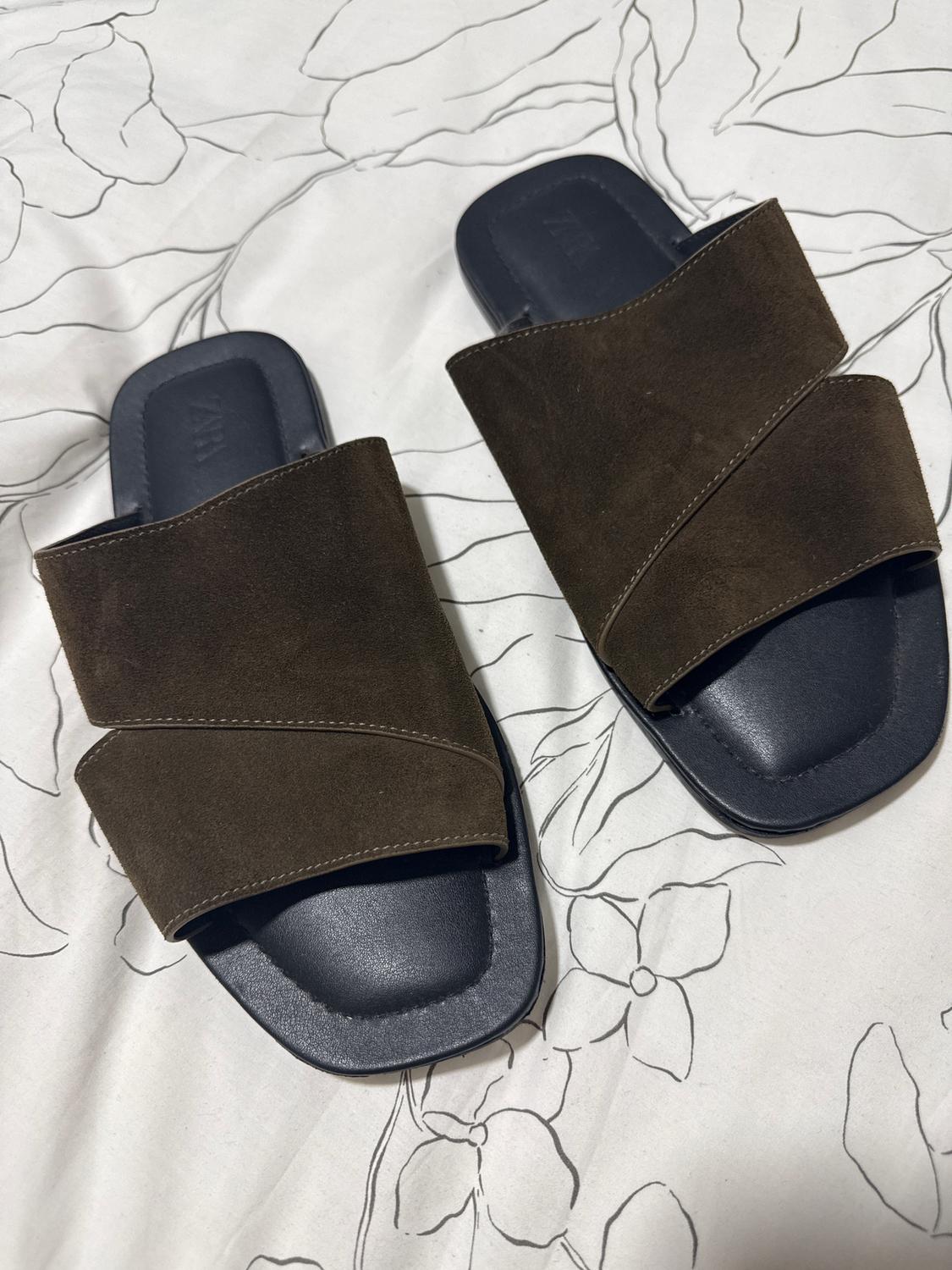 Brown sandals with wide straps on a bed with black and white floral design sheets.