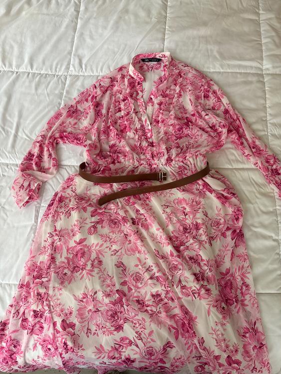 Pink floral dress with brown belt on white quilted bedspread.
