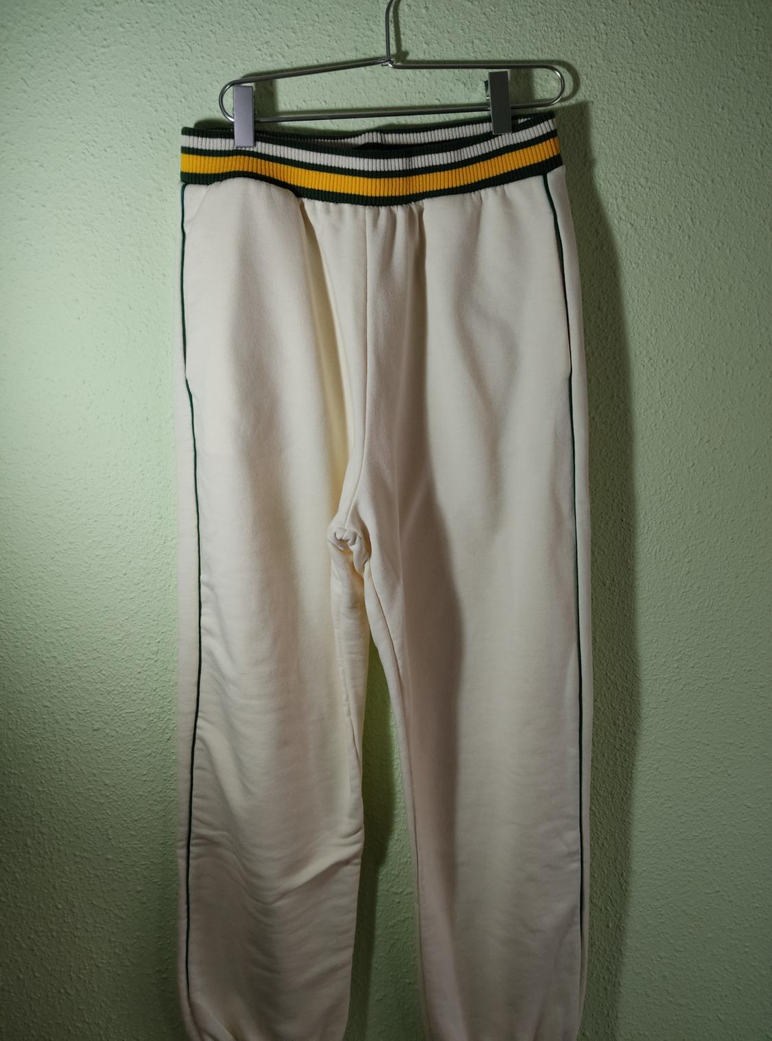 White jogging bottoms hanging on a hanger, with a green and yellow striped elasticated waistband, on a light green background.
