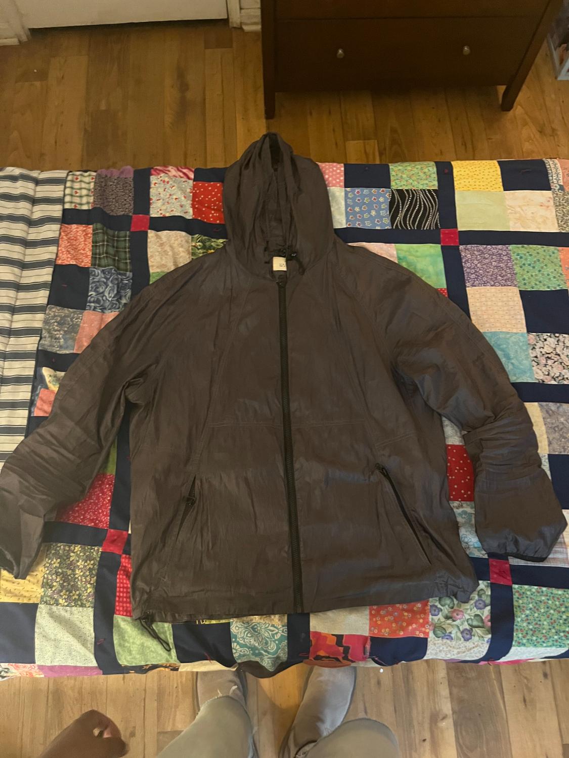 Grey hooded jacket with a black zip on a colourful patchwork quilt in a room with a wooden floor.