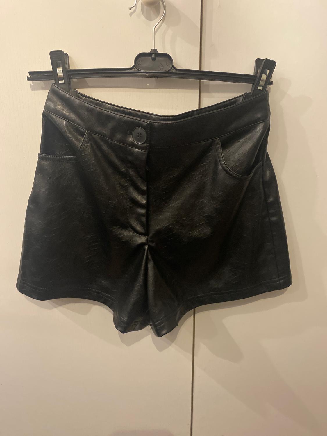 Black synthetic shorts hanging on a black hanger against a white background.