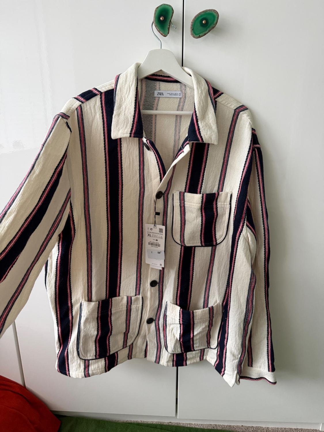 Vertical striped jacket in white, black, and red, hanging on a white hanger. Visible tag with size and price details.