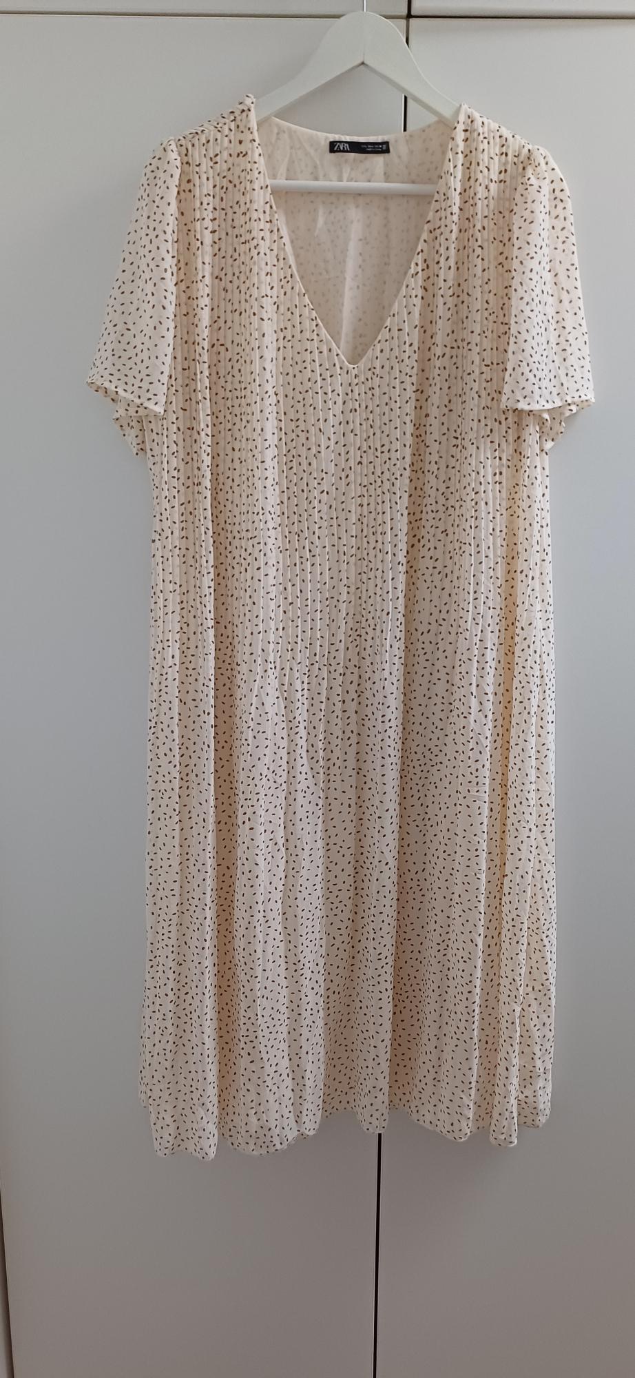 Beige dress with black polka dot print, short sleeves, and a V-neck, hanging on a white hanger against a light background.