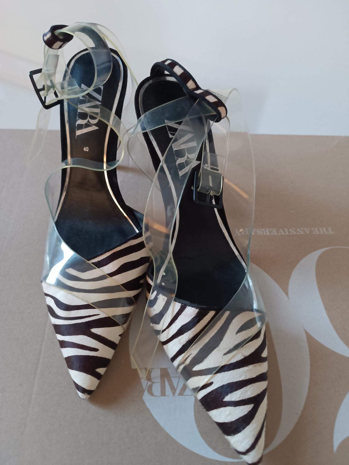 High-heeled shoes with a zebra print and transparent straps on a brown box with the visible Zara logo.