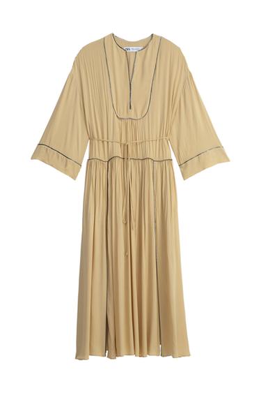 Front view of a beige dress with wide sleeves and pleats, drawstring waist, and dark trim.