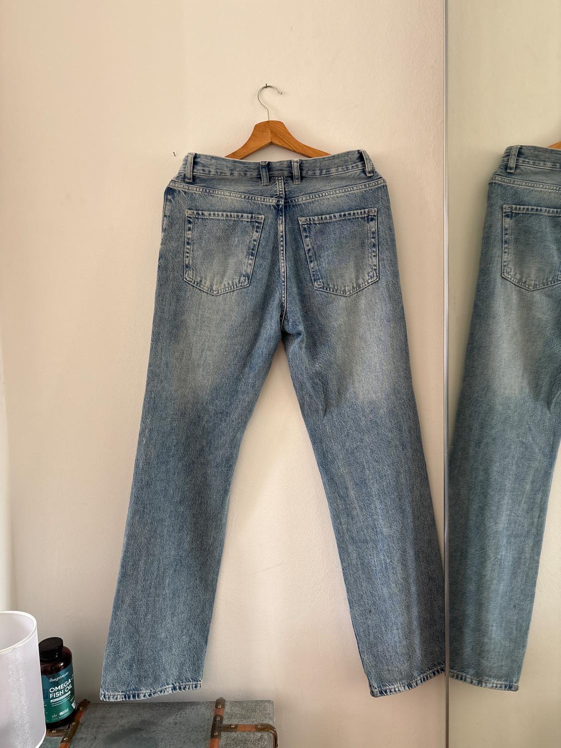 Back of a pair of blue jeans on a hanger against a white wall next to a mirror. Below, a trunk and a tub with the text OMEGA FISH OIL.