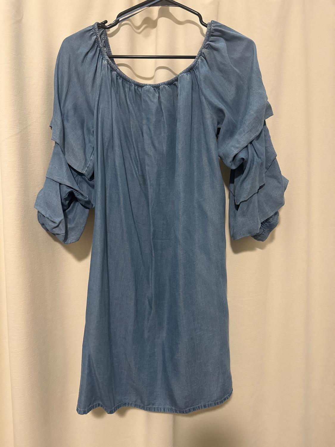 Light blue dress with three-quarter sleeves and frills, hanging on a hanger against a beige background.