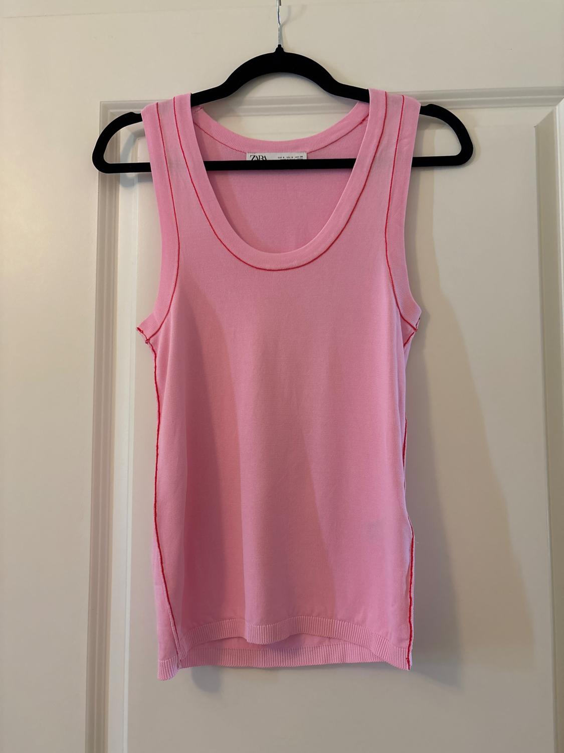 Pink vest top hanging on a black clothes hanger over a white door. Visible label with the text "ZARA".