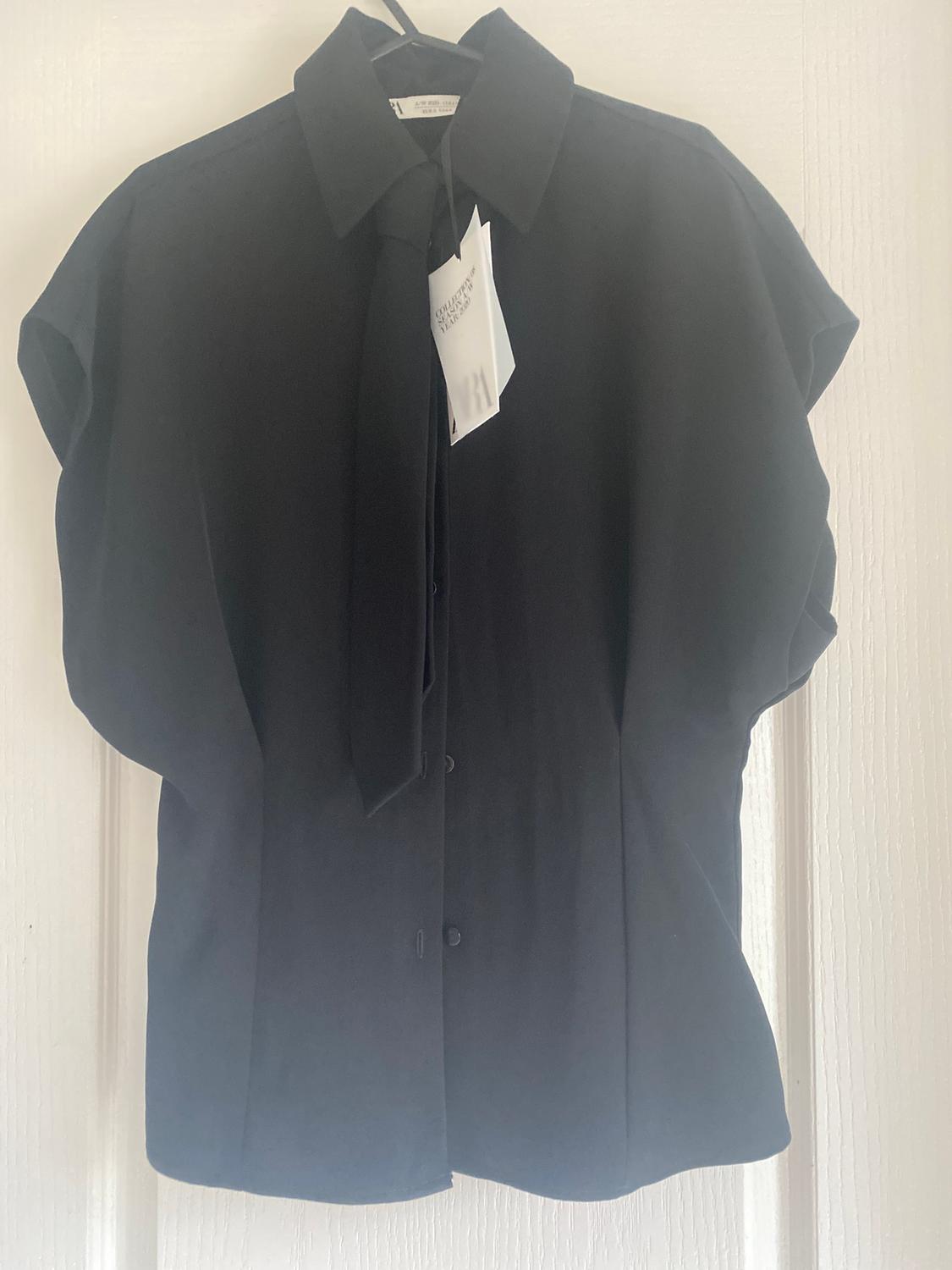 Black short-sleeved shirt hanging on a hanger, with visible tag. White background.