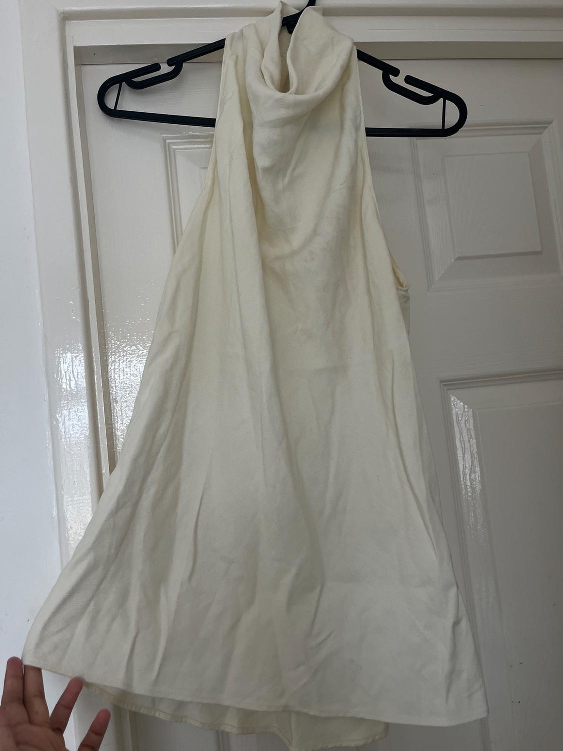 A white top with a high neckline hangs from a black hanger placed over a white door. One hand is holding the bottom of the garment.