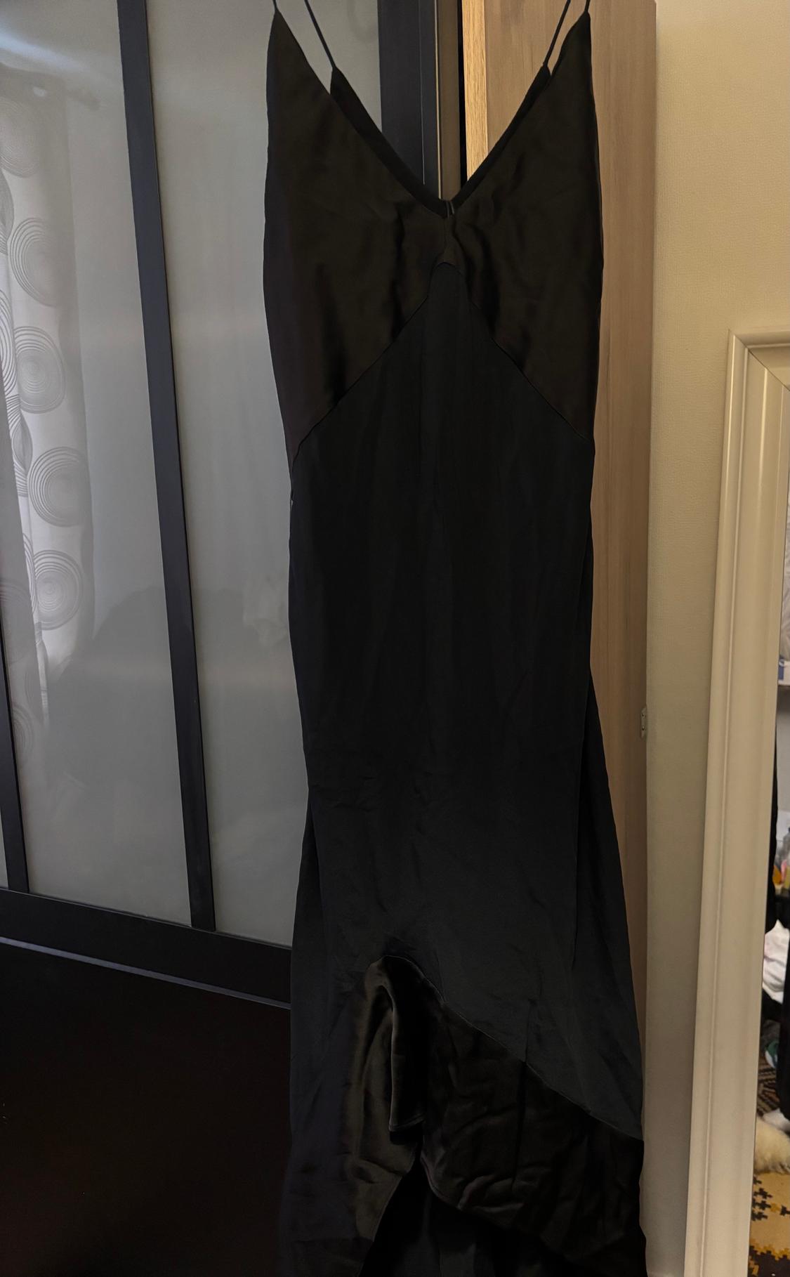 Black spaghetti-strap dress hanging on a wardrobe door. Background with curtain and partially visible mirror.