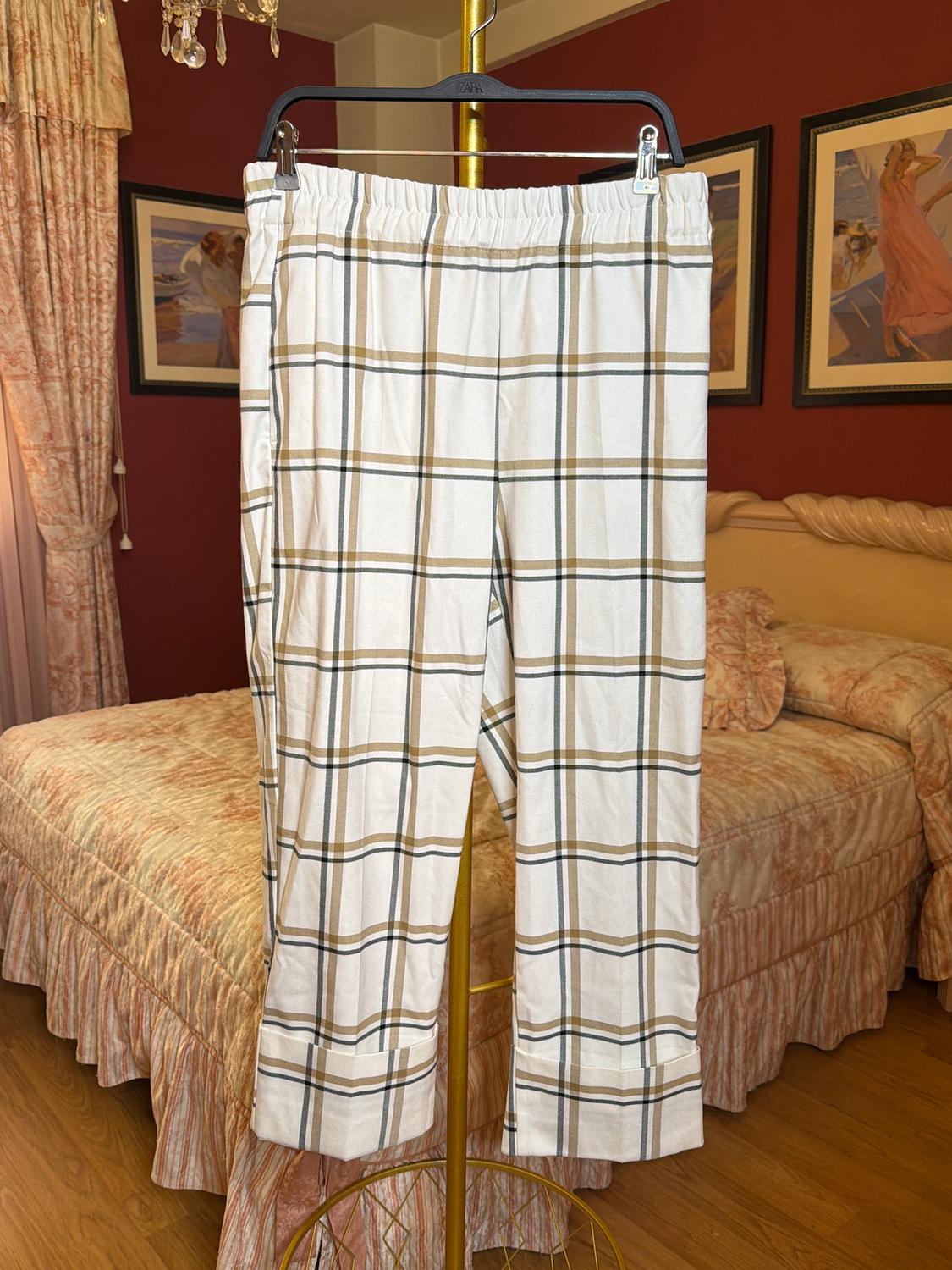 Brown and white checked trousers hanging on a hanger in a bedroom with matching beige curtains and bedspreads.