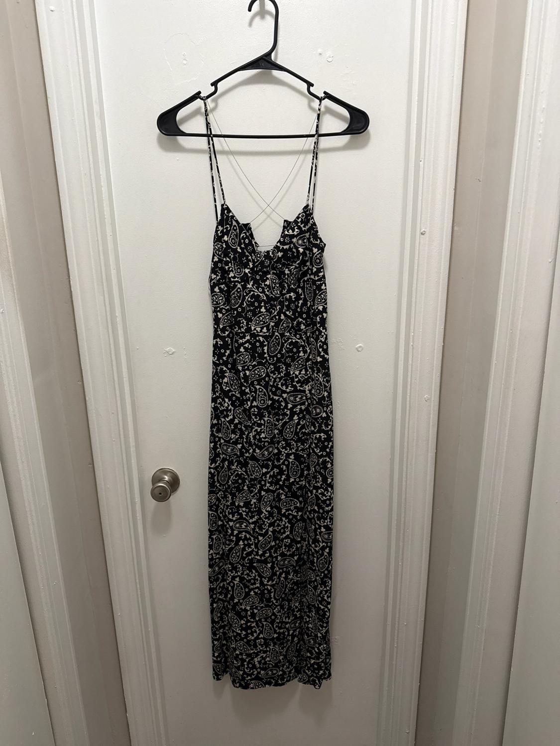 Long black dress with a white print and thin straps, hanging on a black hanger over a white door.