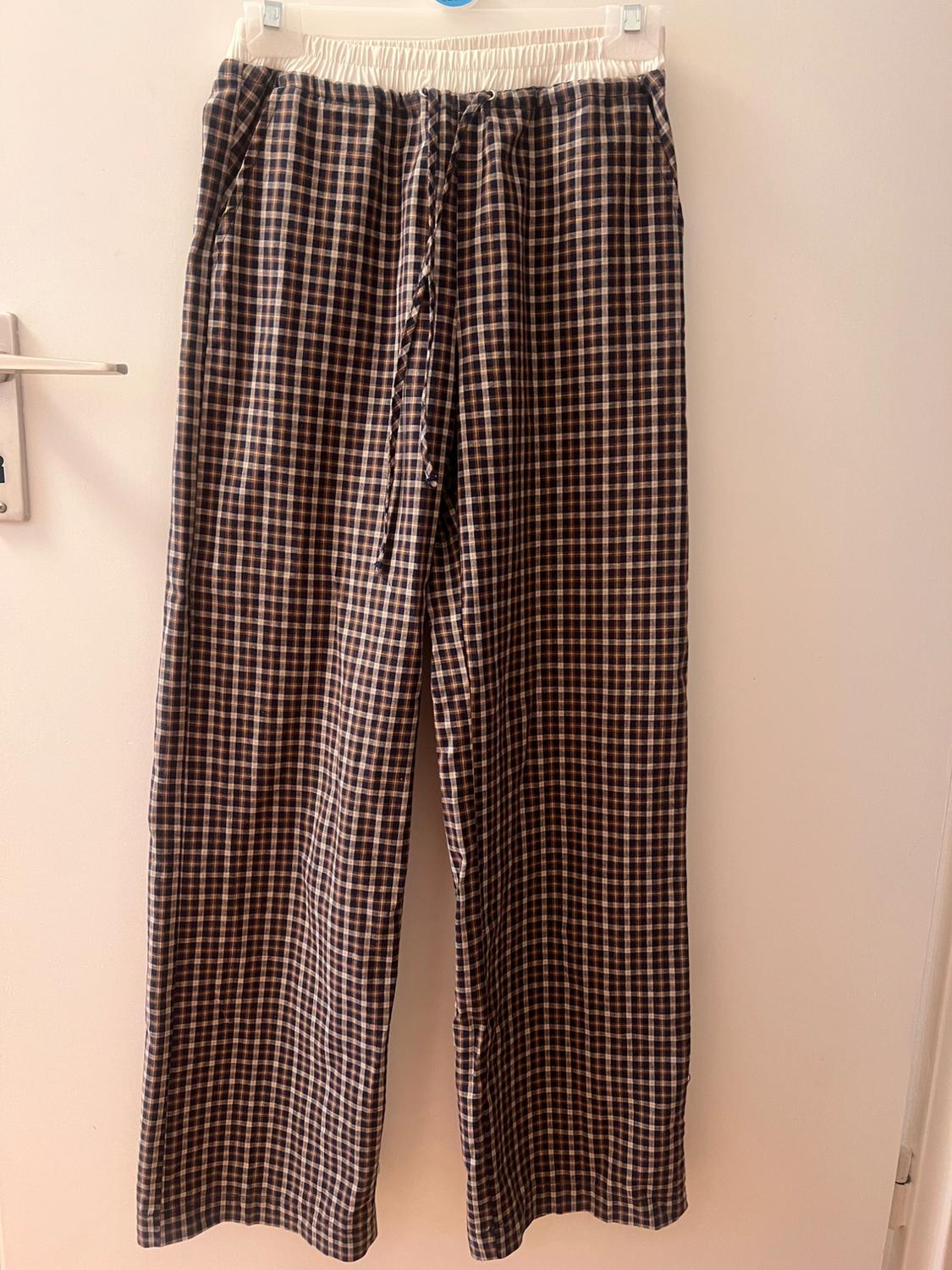 Brown and white checked trousers hung on a hanger, with an elasticated waist and adjustable drawstring, on a white background.