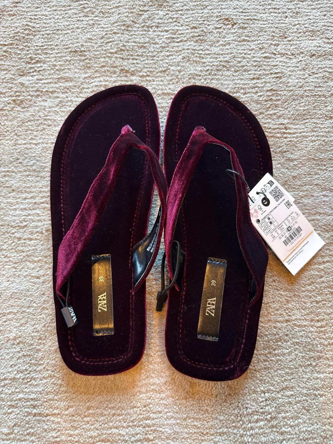 Top view of maroon velvet flip-flops on a light-coloured carpet. The insole reads ZARA 39. They have a white tag.