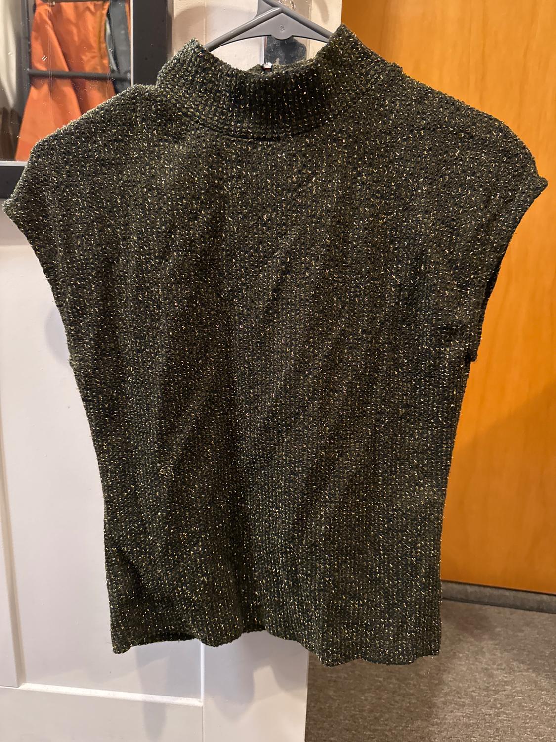 Dark knit high-neck sweater on a hanger, wooden door background and mirror reflecting hanging clothes.