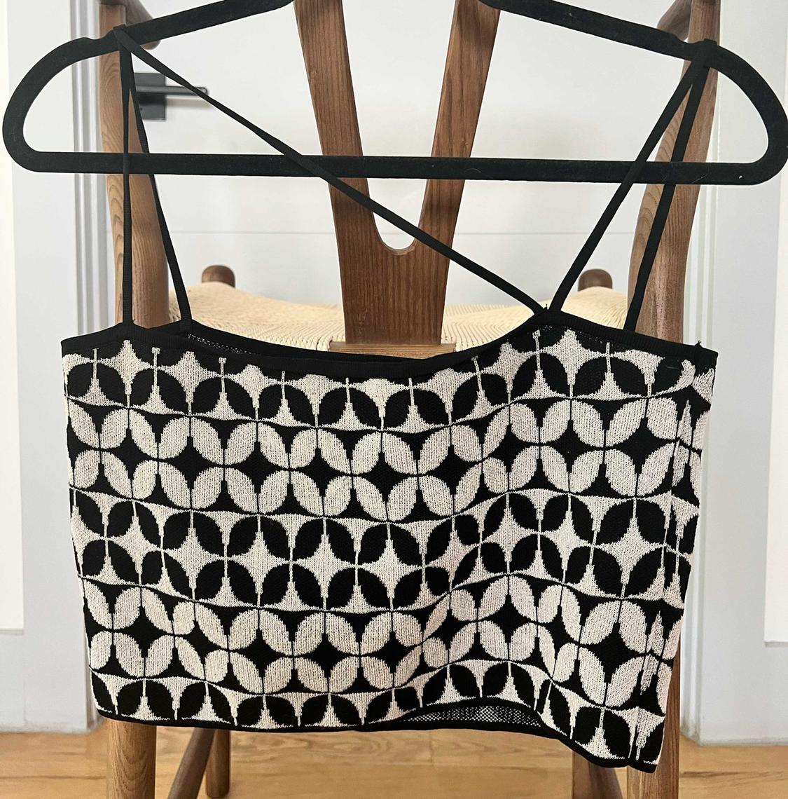 Black and white spaghetti strap top with geometric circle print, hanging on a hanger over a wooden chair.
