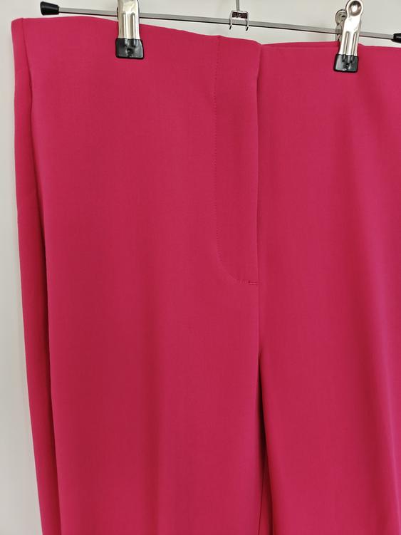 Fuchsia trousers hanging on a hanger with metal clips against a white background.