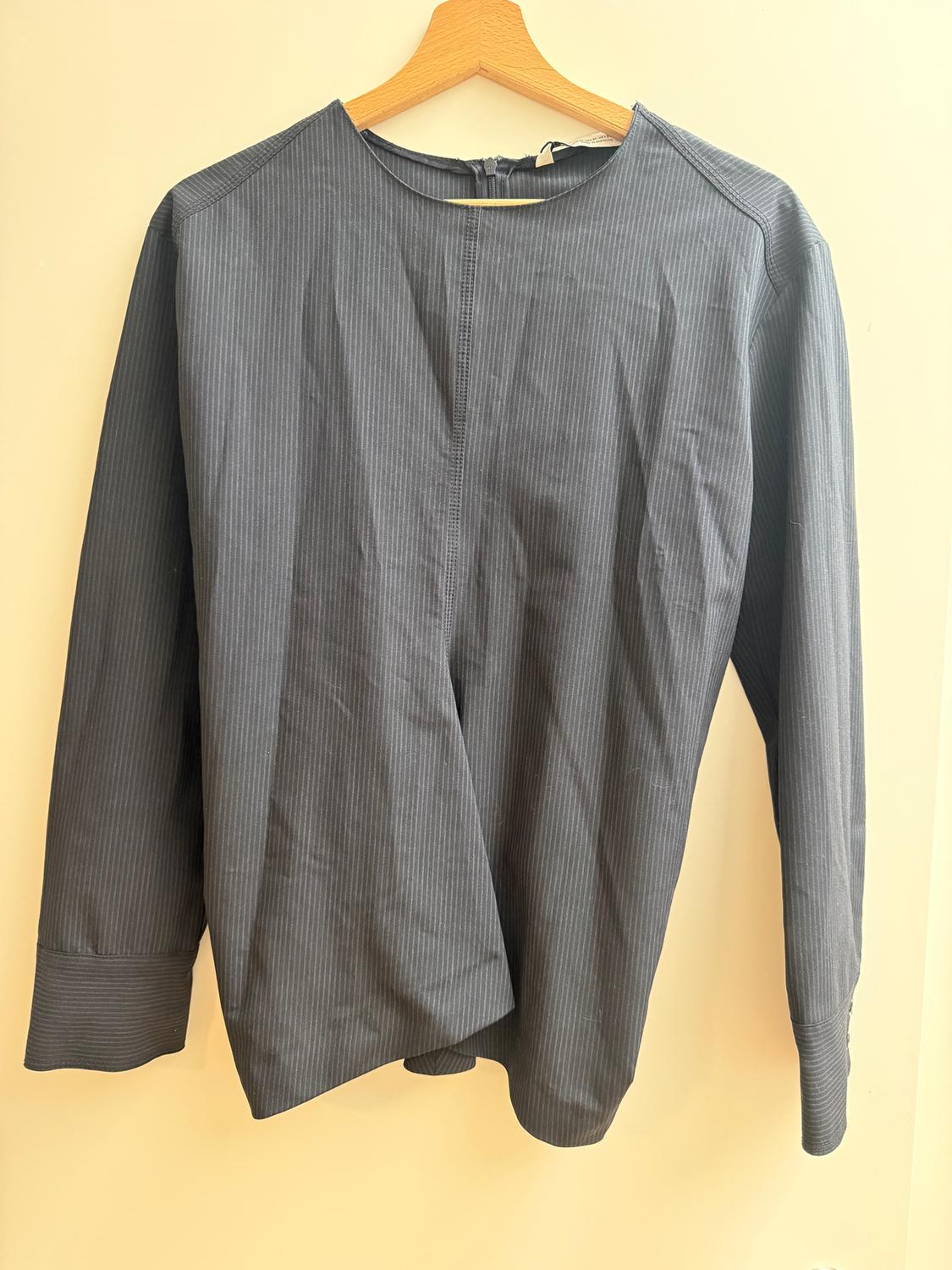 Fine-striped grey shirt hanging on a wooden hanger against a beige background. Long sleeves and a round neck.