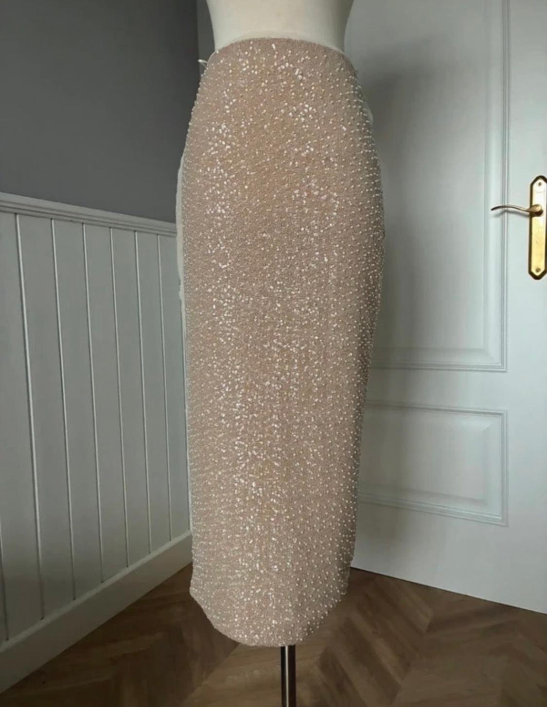 Fitted beige sequin midi skirt on a mannequin, on a wooden floor and white wall with mouldings.