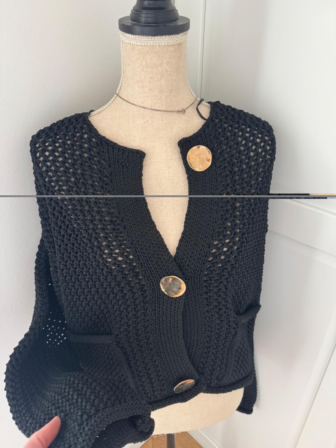 Mannequin with a black knitted waistcoat with large gold buttons, in an indoor setting with natural light.