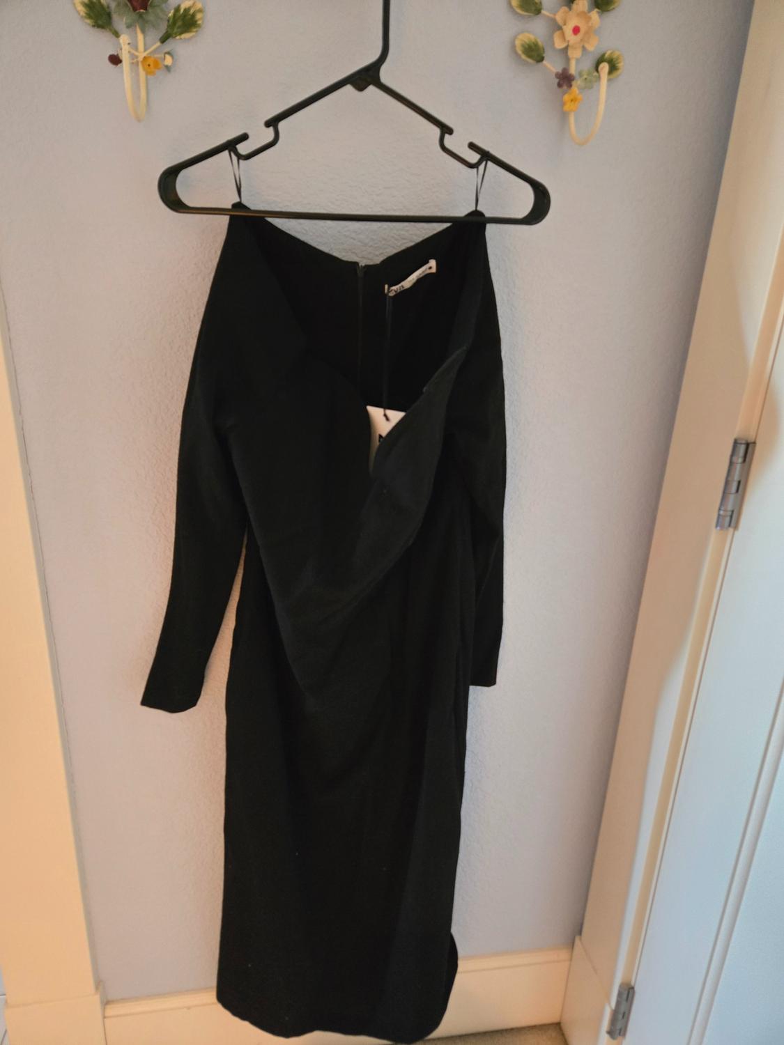 Long-sleeved black dress hanging on a black hanger against a light blue wall, decorated with ceramic flowers.