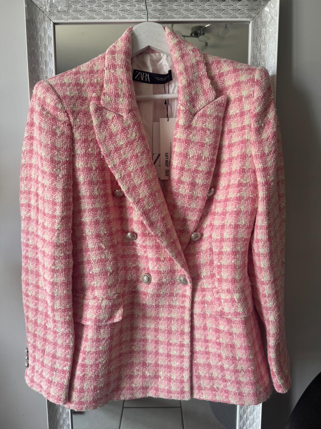 Pink and white checked jacket with silver buttons, hanging on a hanger in front of a mirror. Visible label: ZARA.