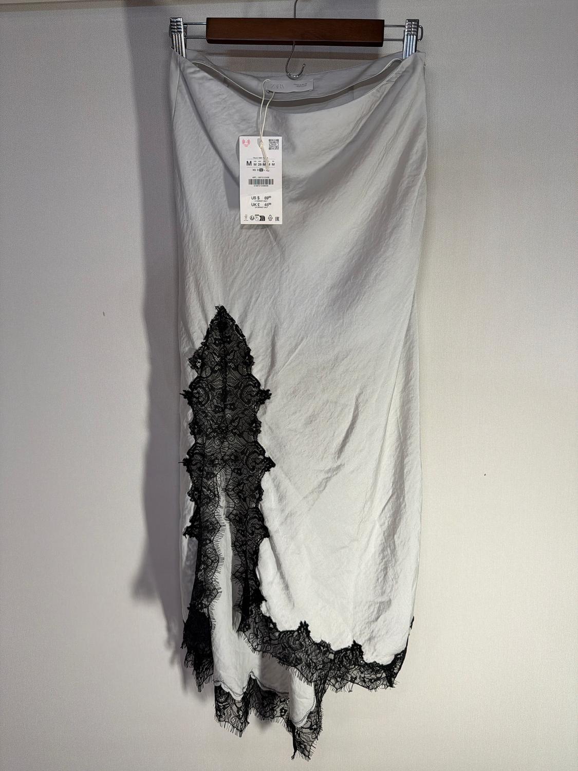 White skirt hanging with black lace on the hem and visible tag. Neutral background.