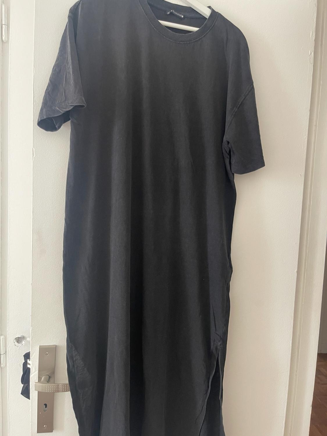 Black long t-shirt style dress with short sleeves and side slits, hanging on a hanger on a white door.