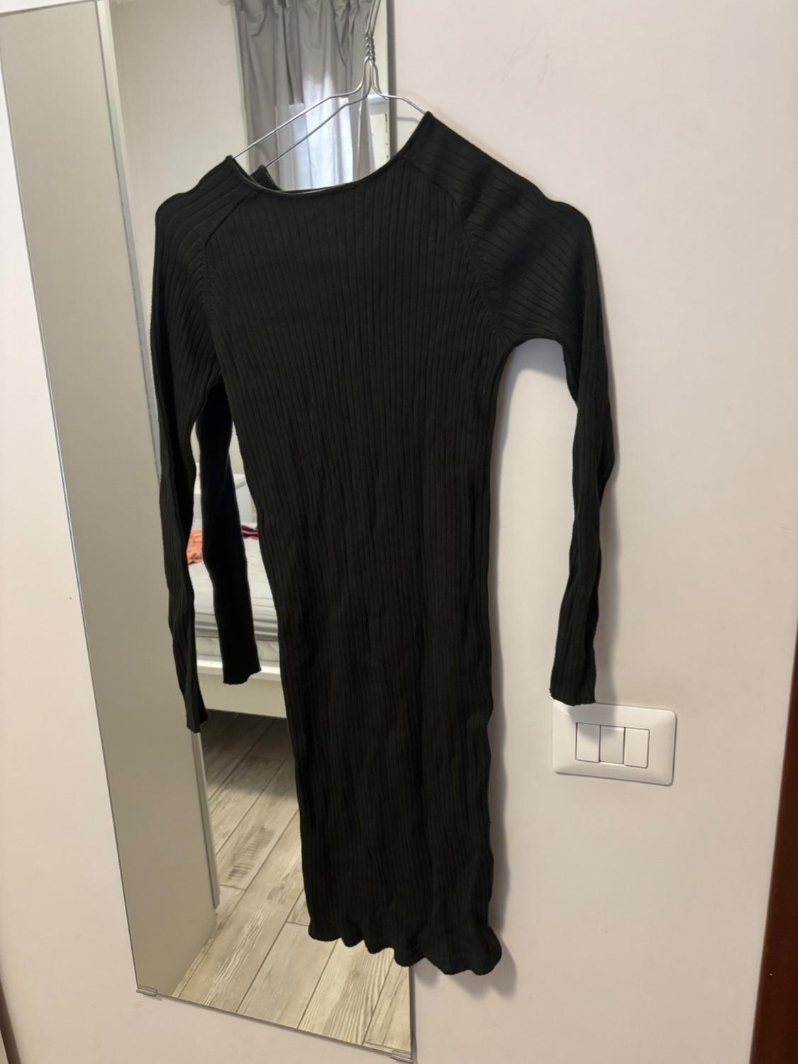 Black ribbed-knit long-sleeved dress hanging on a hanger against a white wall beside a mirror reflecting a room.