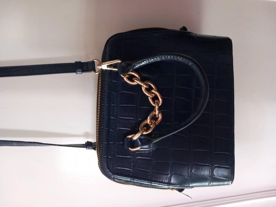 Black croc-effect handbag with a short handle, gold chain detail and long strap, set against a white background.