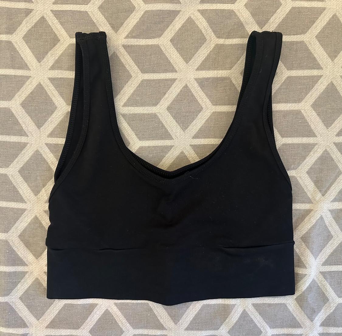 Black sleeveless sports top with wide straps in flat construction on a fabric backdrop with a geometric pattern in grey and white.