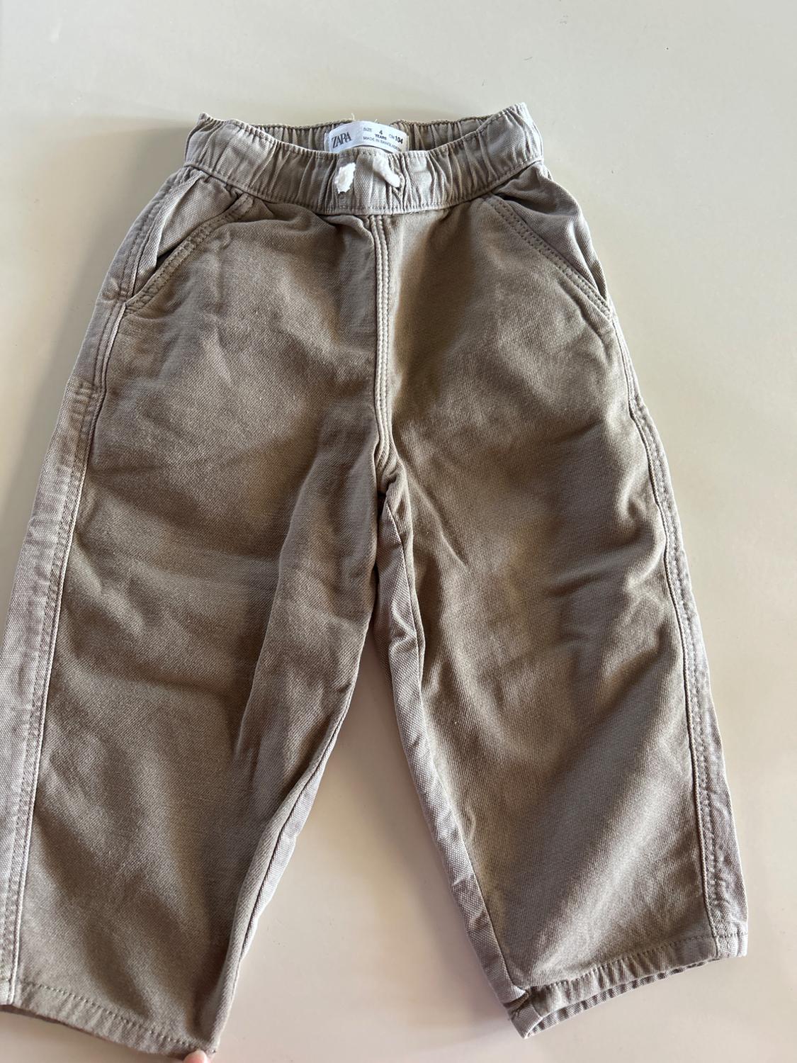 Beige soft fabric trousers with an elasticated waist and side pockets, on a light background. Visible label at the waist.