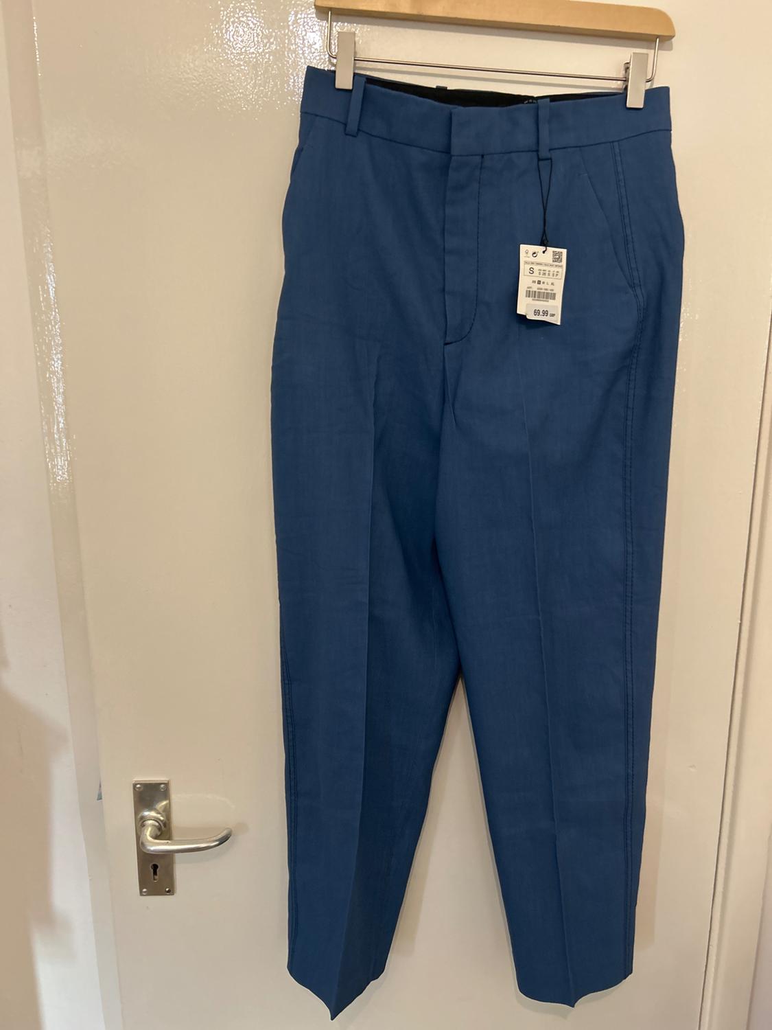 Blue trousers hanging on a wooden hanger over a white door. Visible tag with price of 69.99.