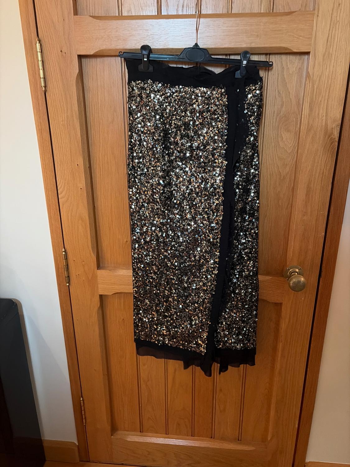 Shimmering gold and silver sequin skirt hanging on a light wooden door.