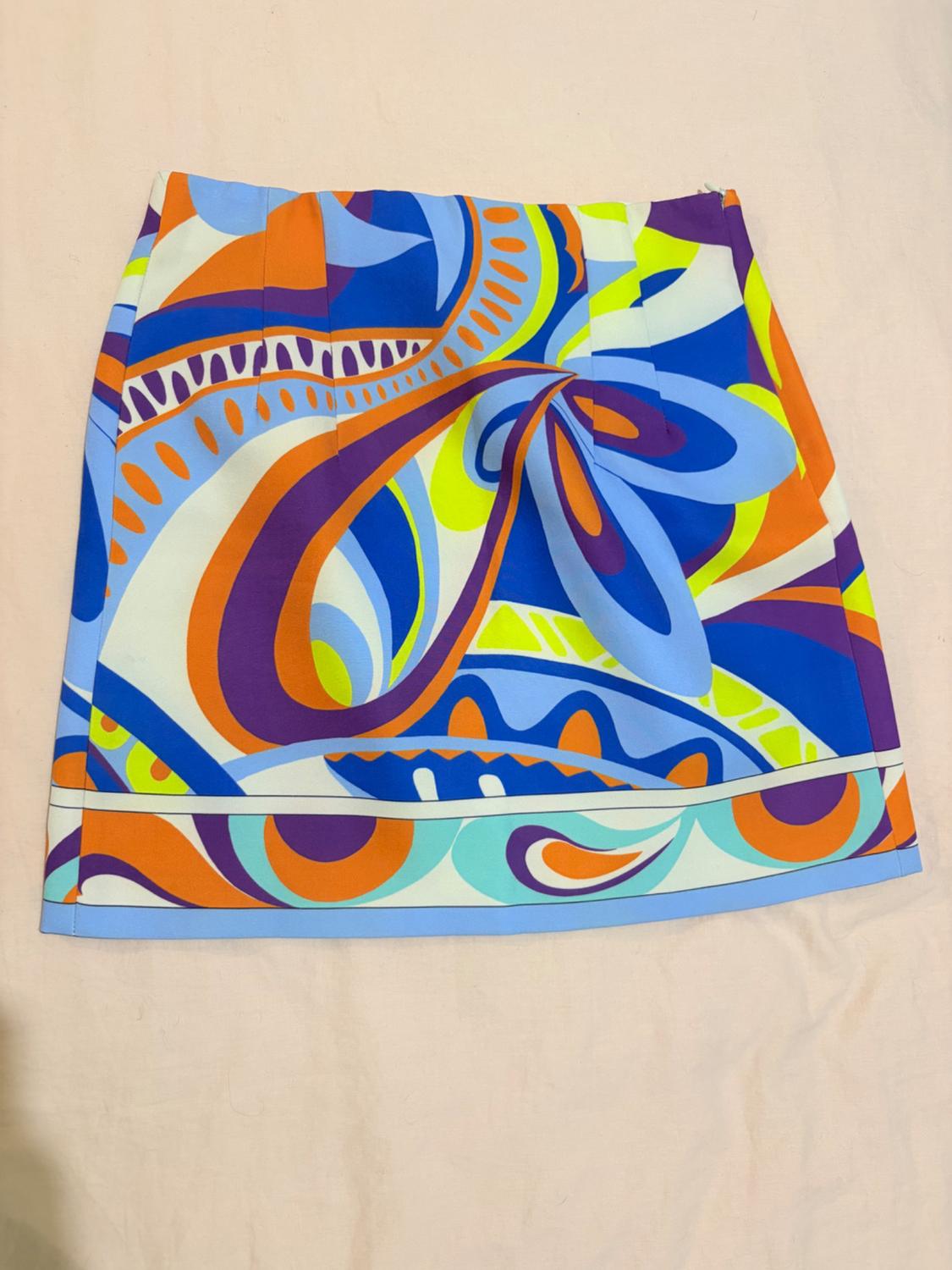 Short skirt with a retro abstract wavy print in blue, orange, purple and neon yellow, on a light fabric background.