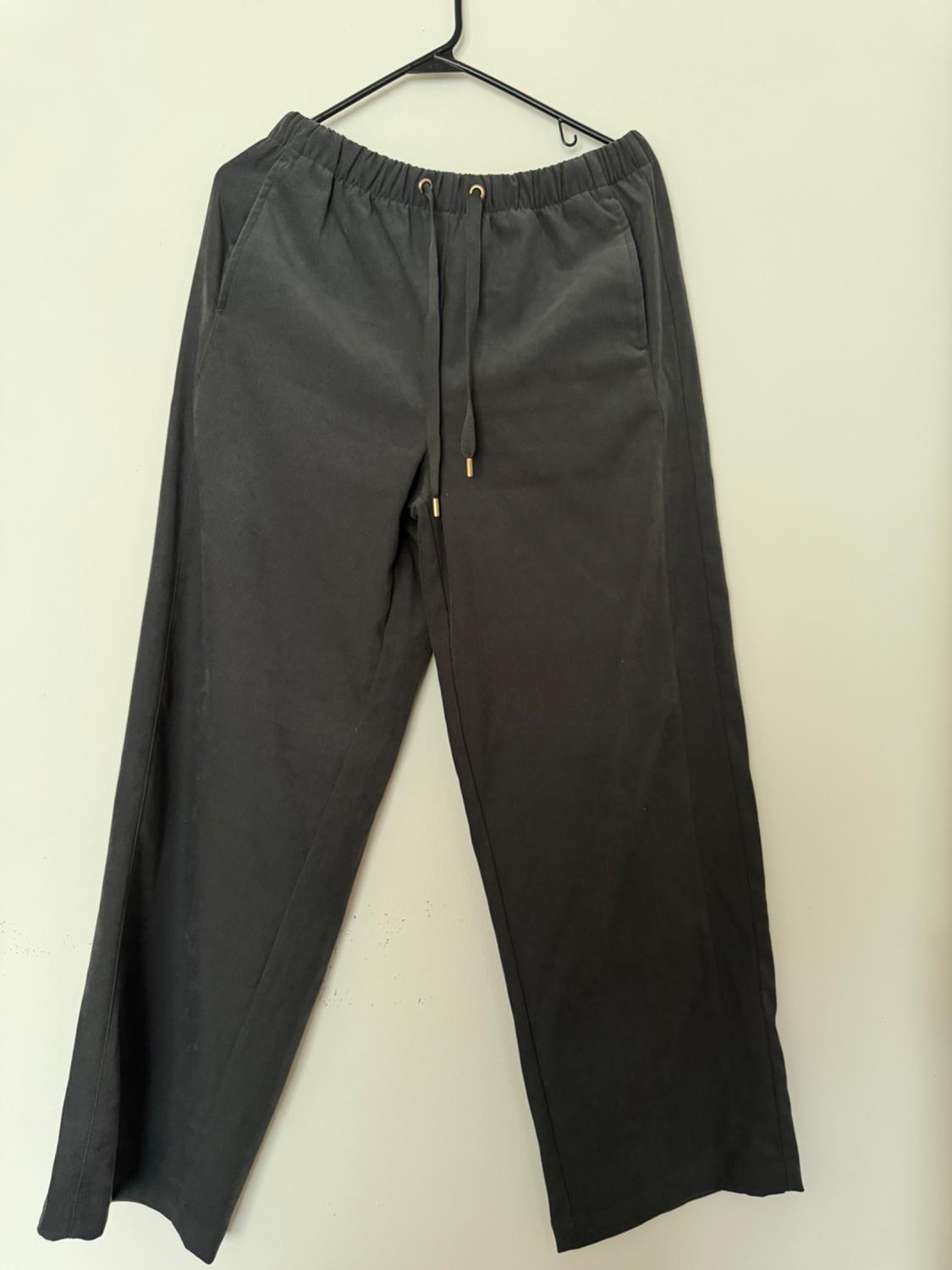 Black pants hanging on a hanger, with an elastic waistband and adjustable drawstrings, against a white background.