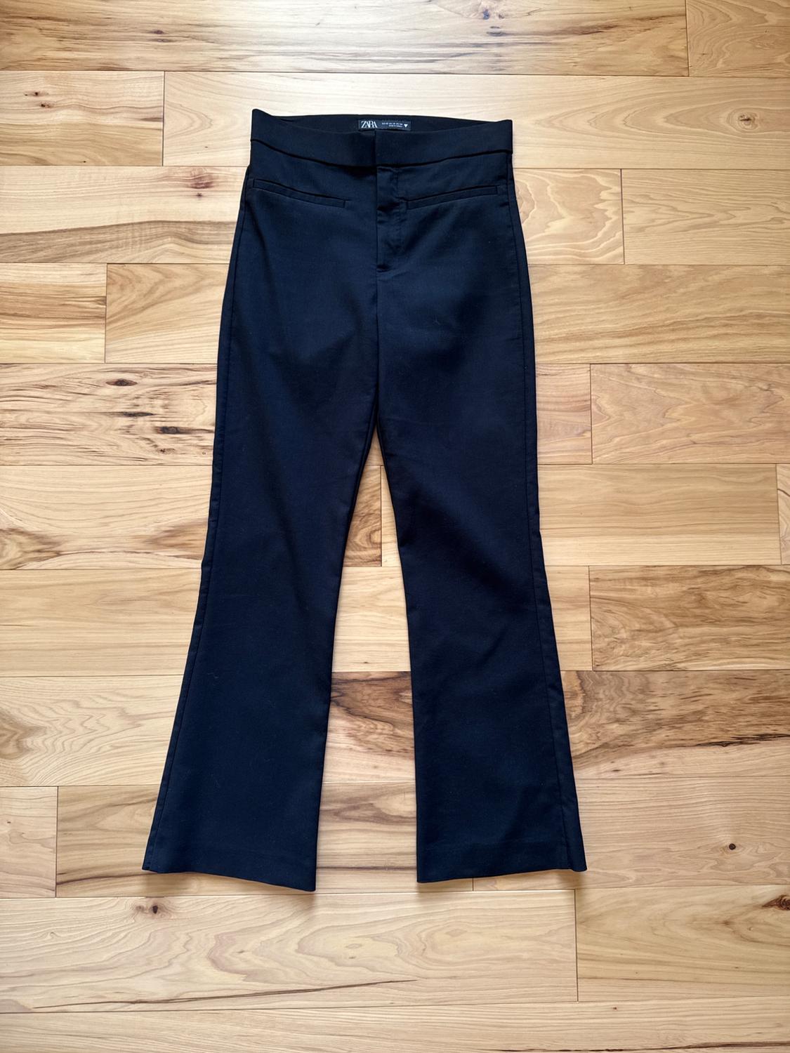 Black flared pants with front pockets on a light wood floor. Visible label on the waistband with the Zara logo.