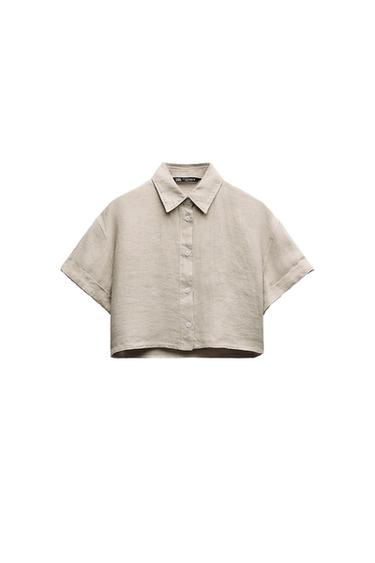 Front view of a short beige shirt with a classic collar and central button fastening.