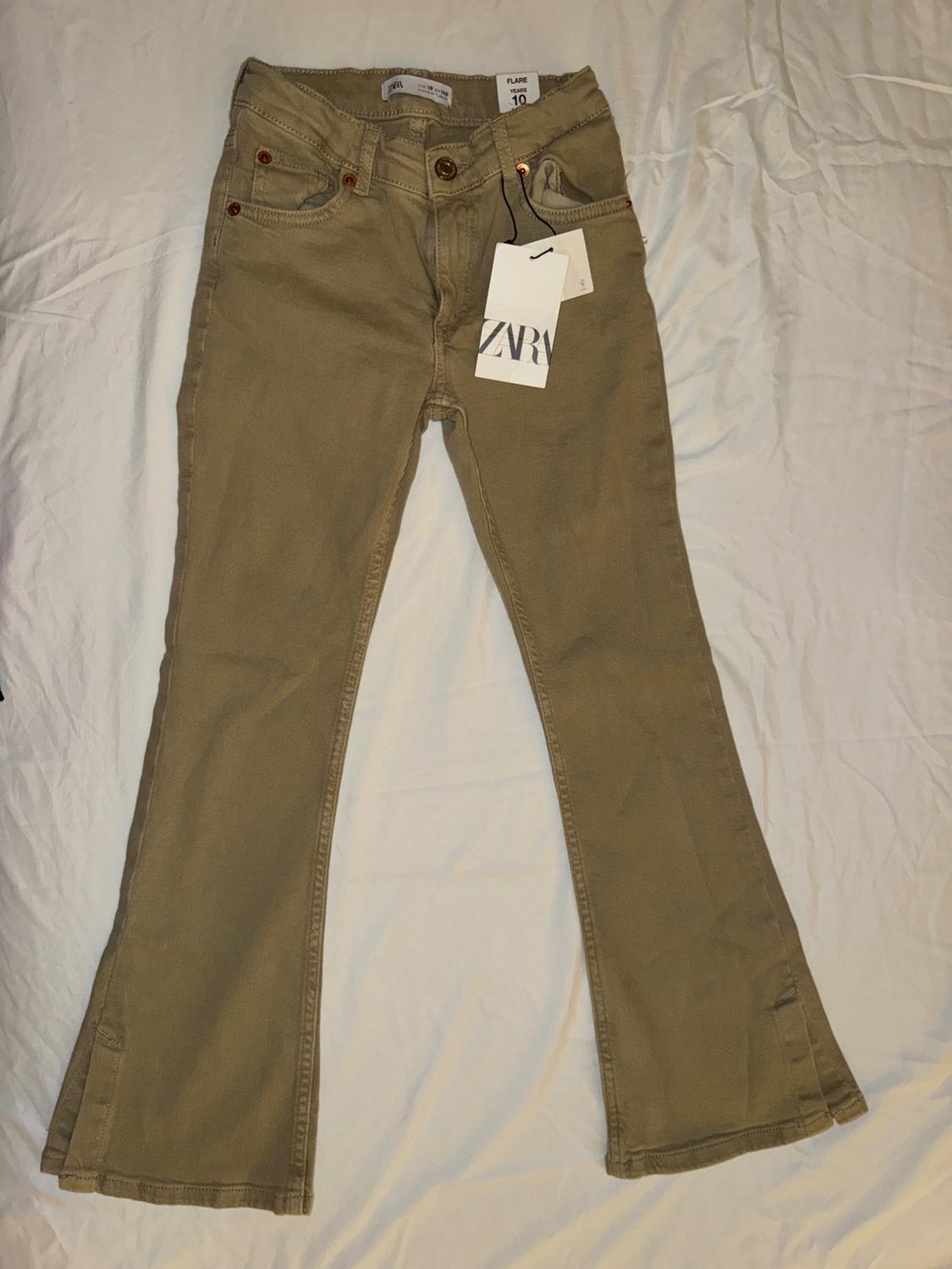 Front view of beige bell-bottom pants with front pockets and visible button.